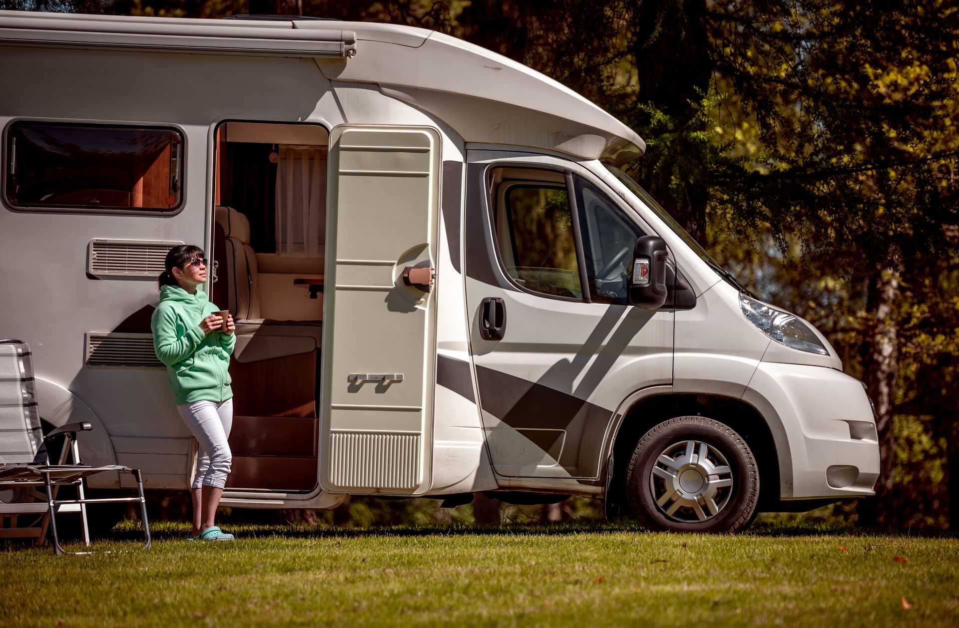 White camper van parked on grass, with a person standing by the open side door at a campsite.
