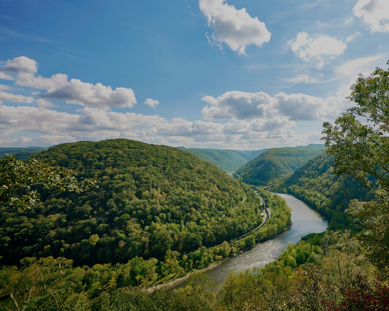 River winding through lush green forested hills under a blue sky with scattered clouds