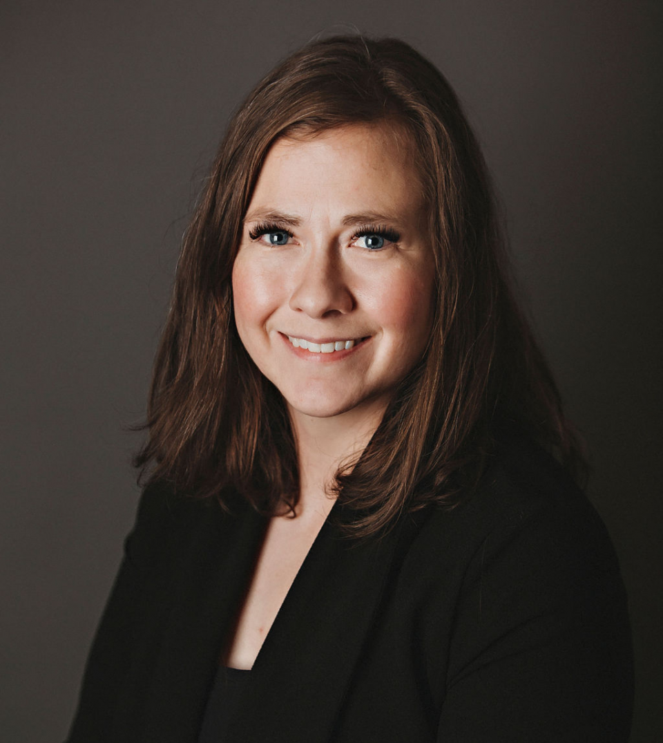 Studio headshot of a smiling woman in a black blazer against a dark background