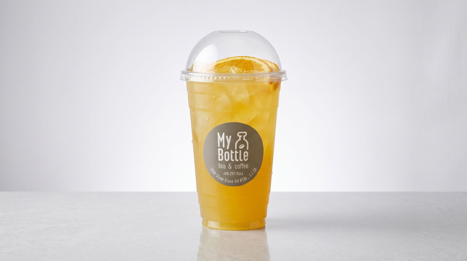 Yellow iced drink in a clear plastic cup with a dome lid and straw on a white background