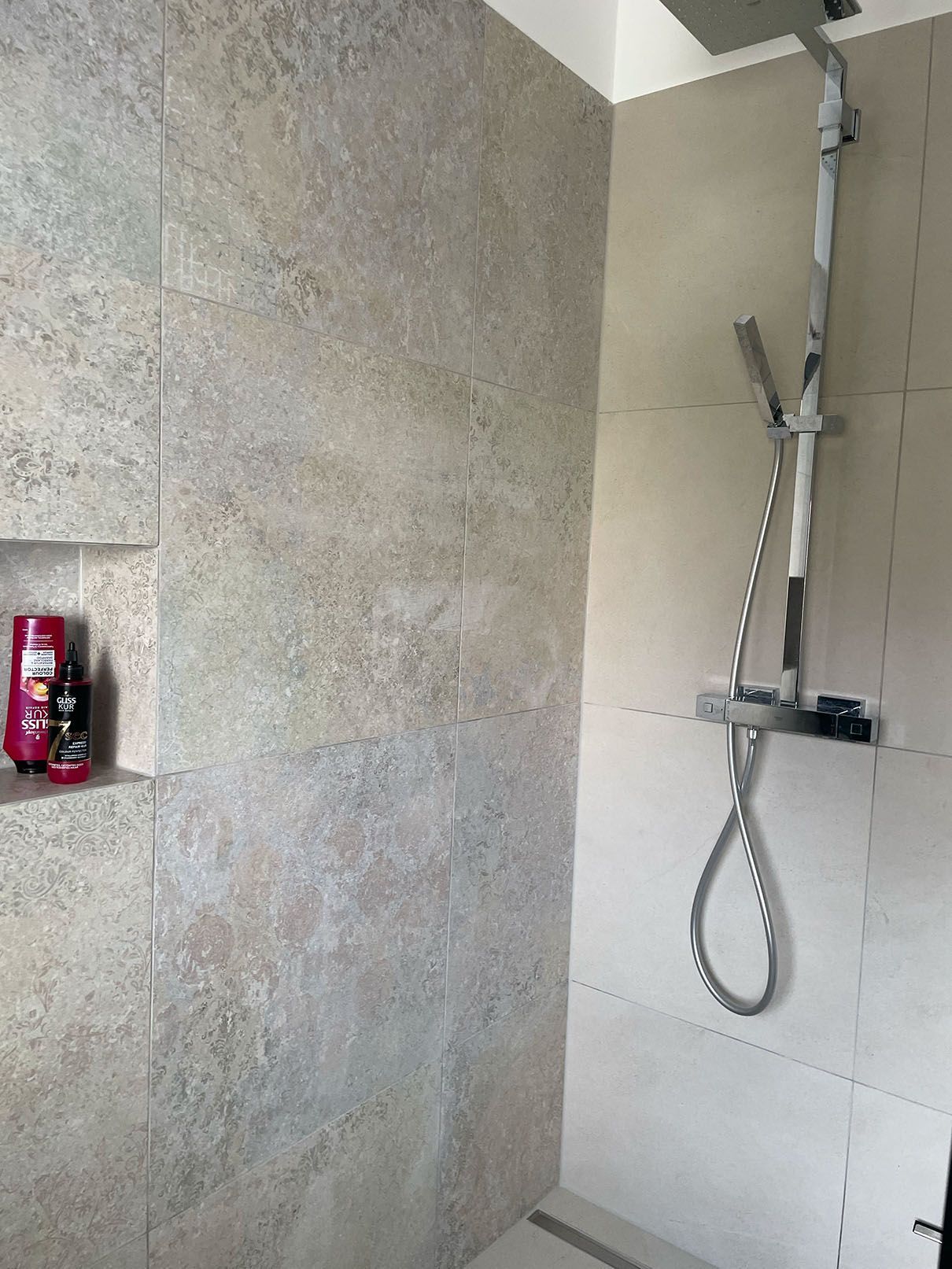 Eine Dusche mit Duschkopf und einer Shampooflasche auf einem Regal.