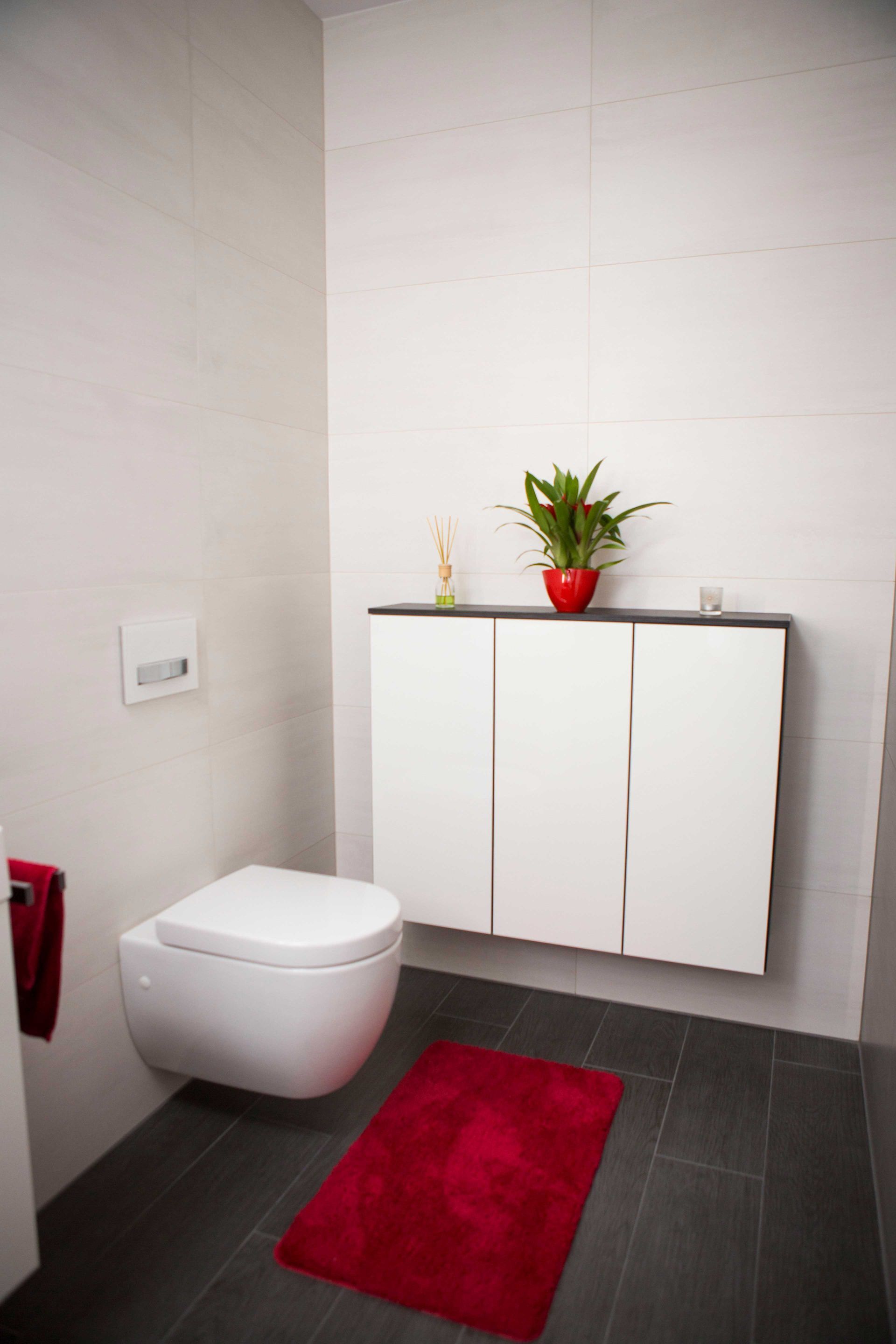 Ein Badezimmer mit Toilette und einem roten Teppich auf dem Fliesenboden.