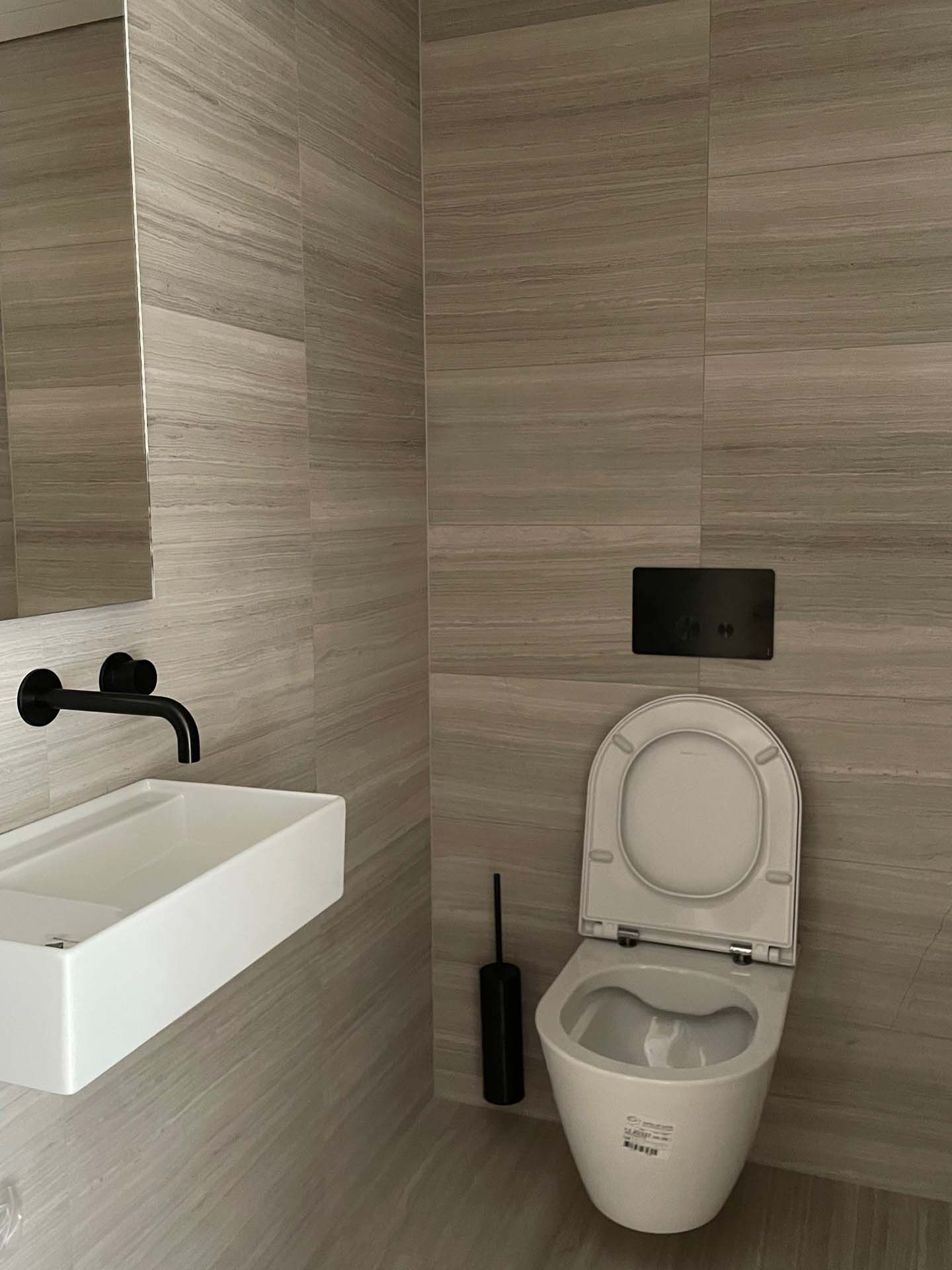 Ein Badezimmer mit Wandfliesen in Holzoptik, Toilette, Waschbecken und Spiegel.