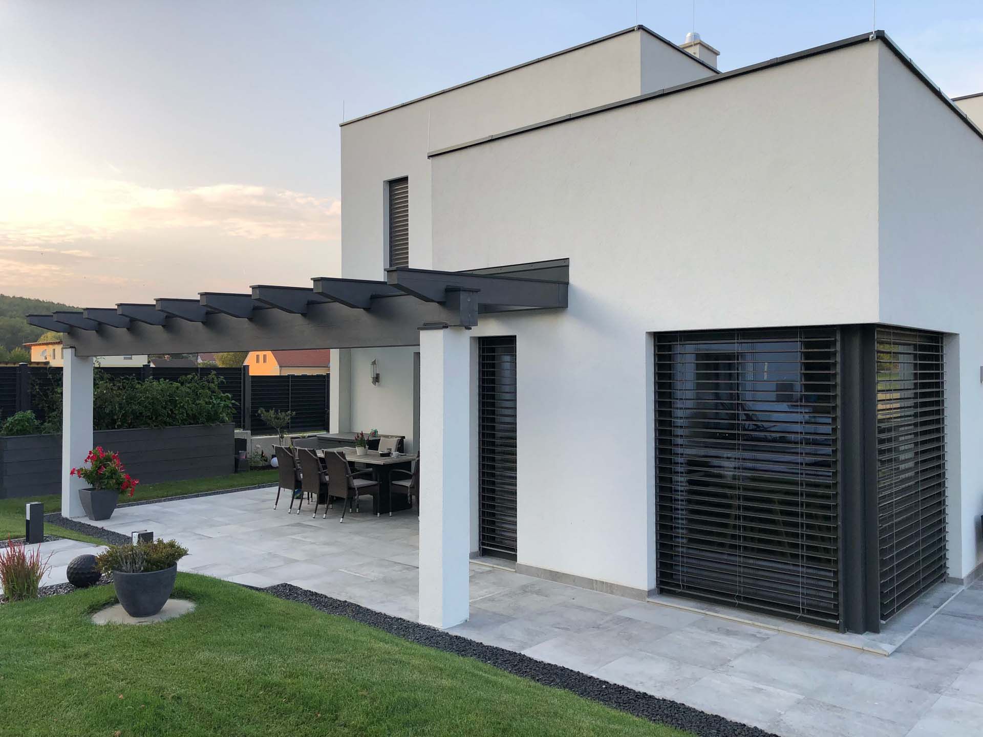 Ein weißes Haus mit einer Pergola und einer Terrasse davor.