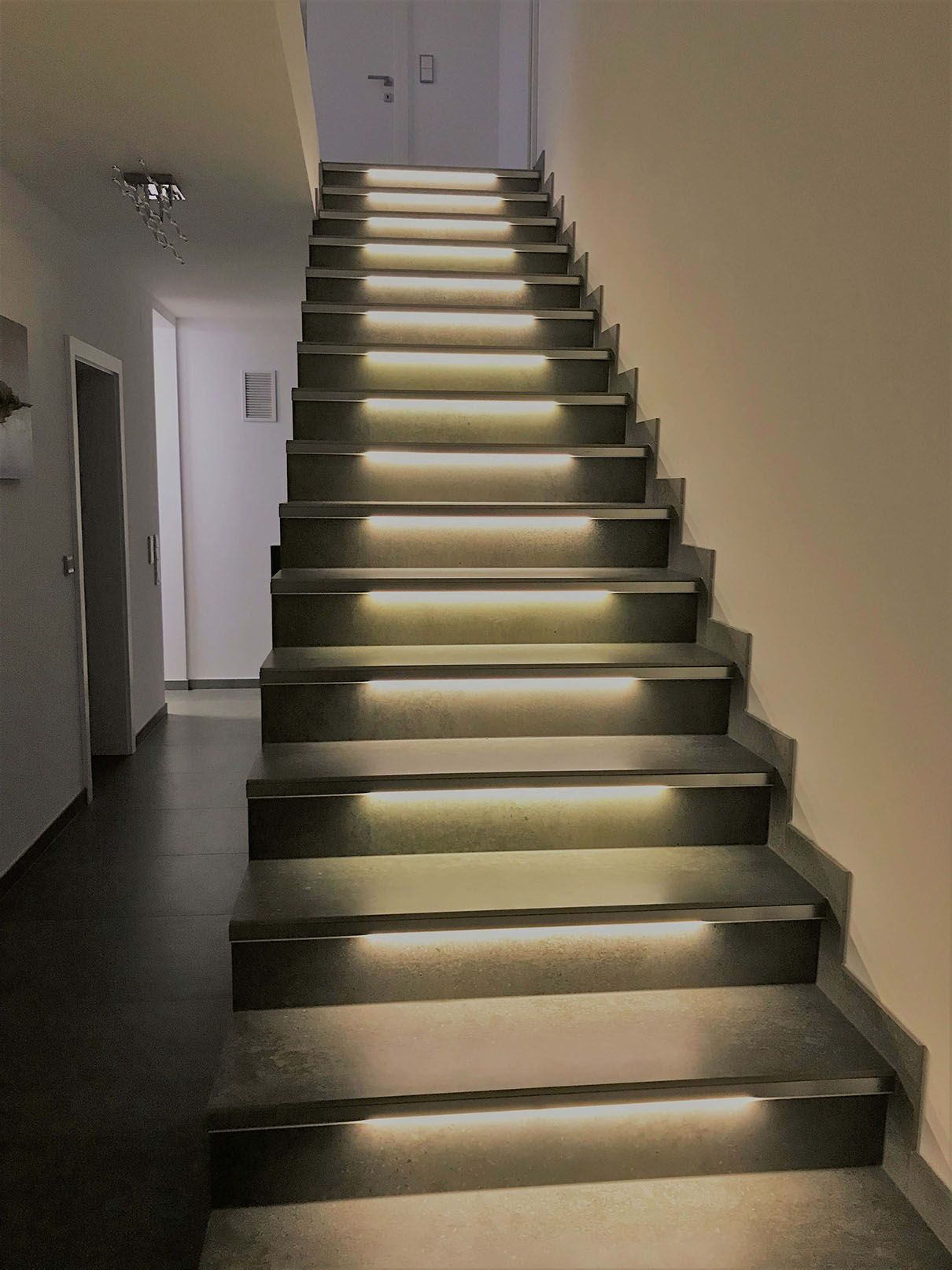 Eine beleuchtete Treppe aus Natursteinfliesen in einem Flur.