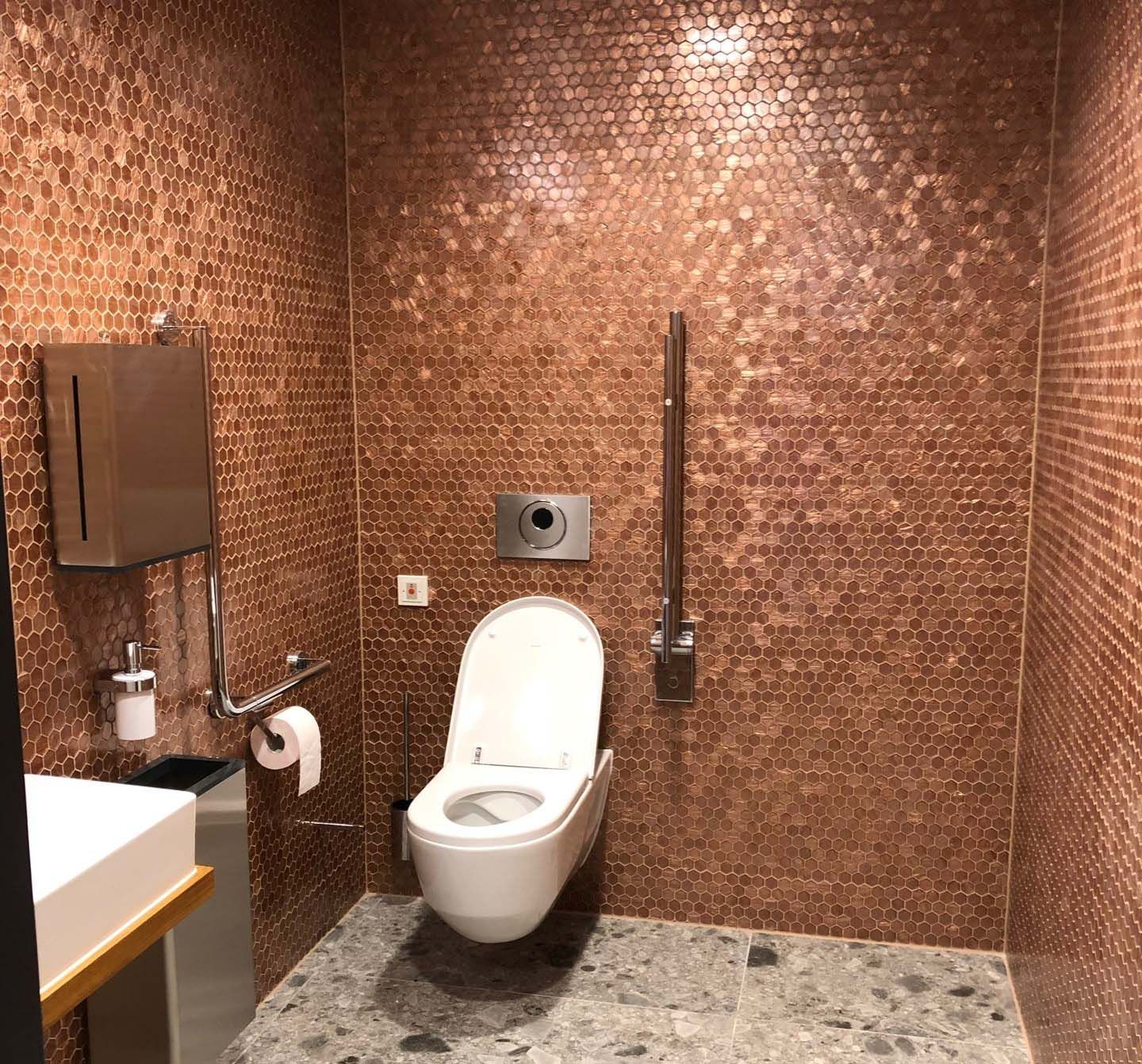 Ein Badezimmer mit roten Fliesen im Mosaikmuster, mit Toilette und Waschbecken.