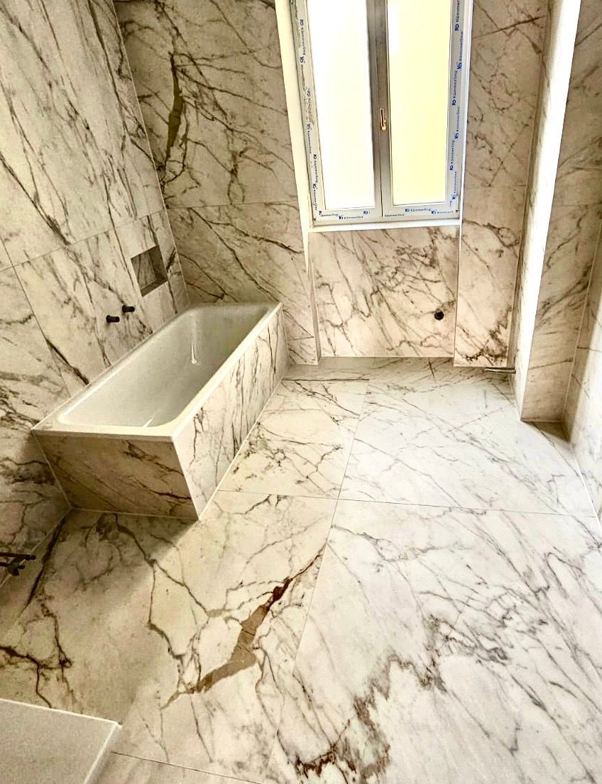 Ein Badezimmer mit Badewanne und Duschkopf, auf den Wänden sind Marmorfliesen