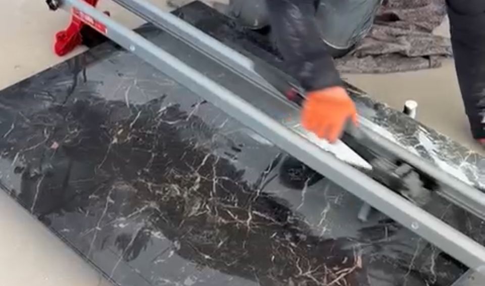 Eine Person schneidet eine Fliese mit einem Fliesenschneider.