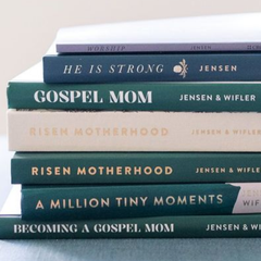 Stack of blue and beige books on motherhood and faith, including “Gospel Mom” and “Risen Motherhood”