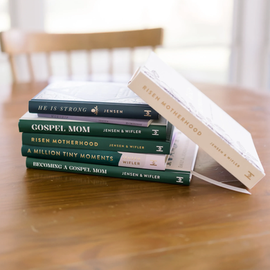 Stack of books on a wooden table, with one white book leaning against the pile in a bright room.