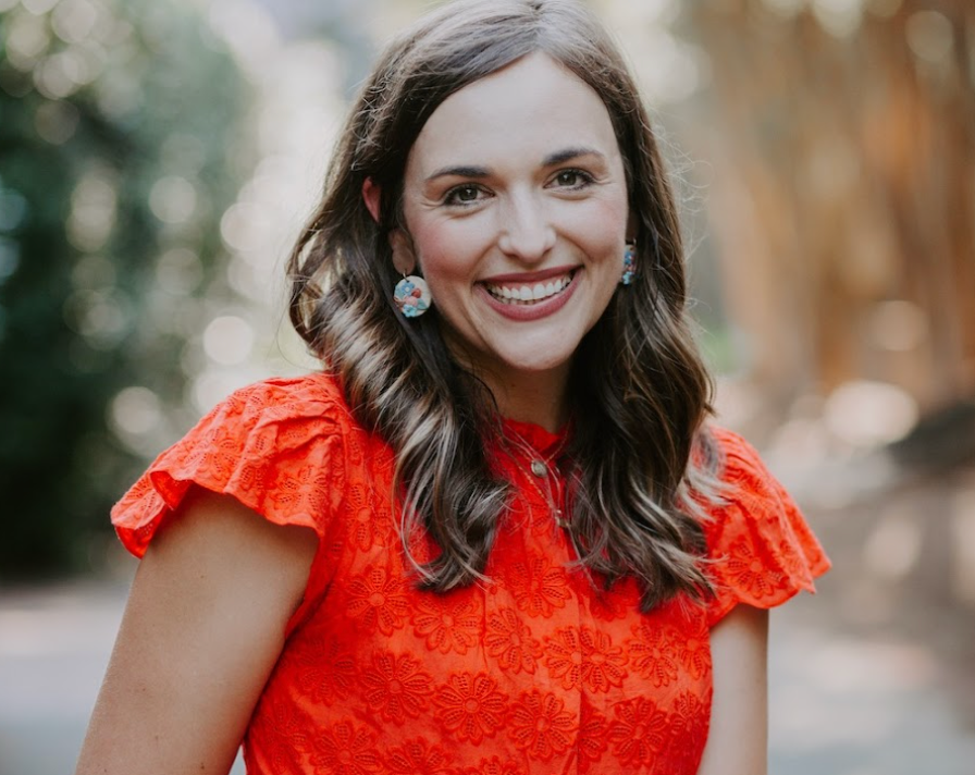 Smiling woman in a bright red dress standing outdoors with a blurred natural background