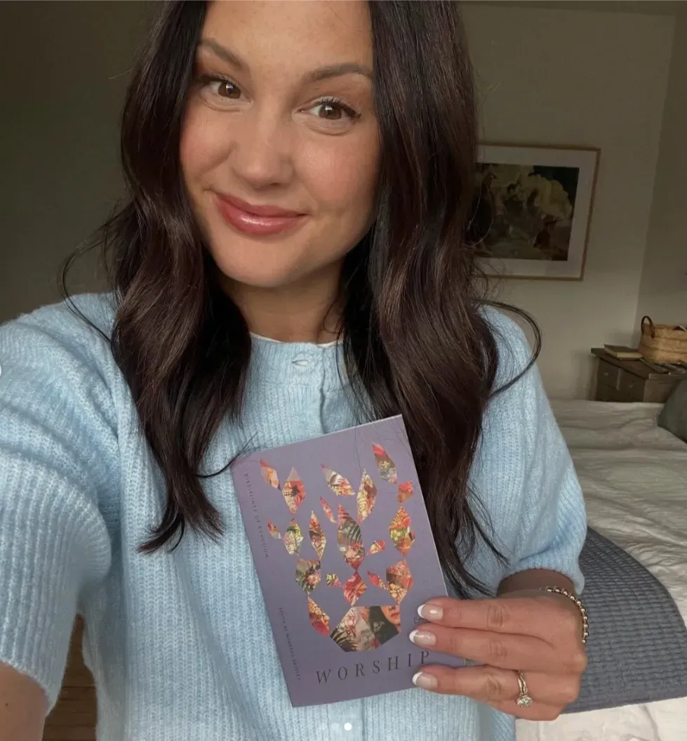 Woman in a light blue sweater holding a purple floral card indoors, smiling at the camera.