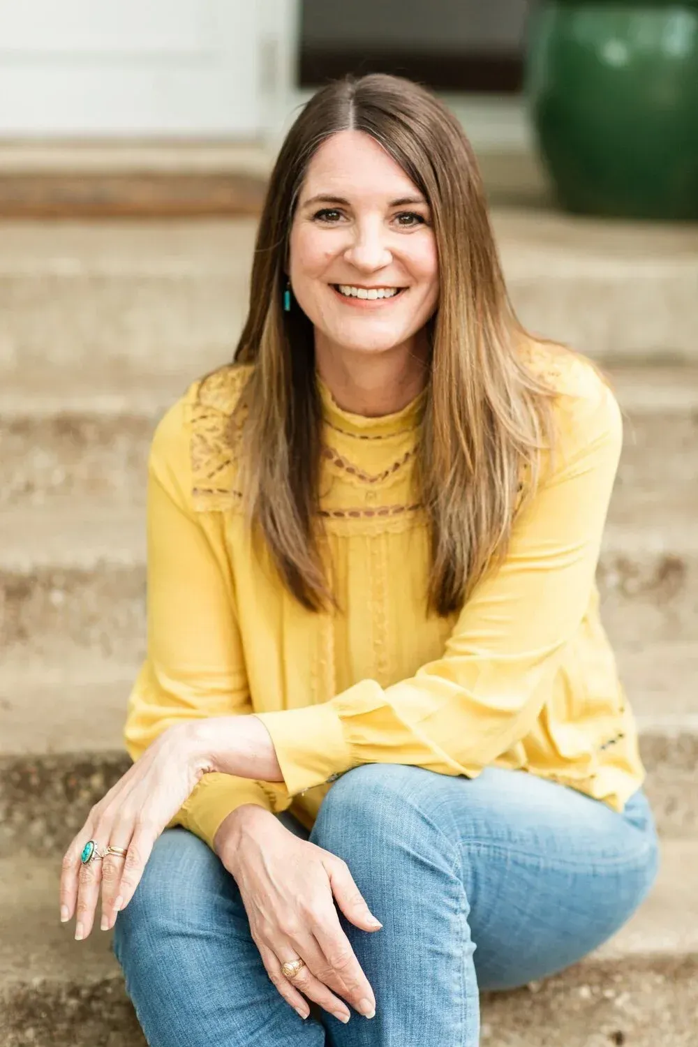 Smiling woman in a yellow blouse and jeans sitting on stone steps outdoors