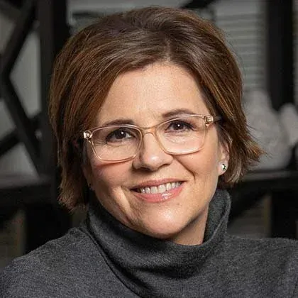 Portrait of a smiling person wearing glasses and a dark turtleneck sweater against a blurred background