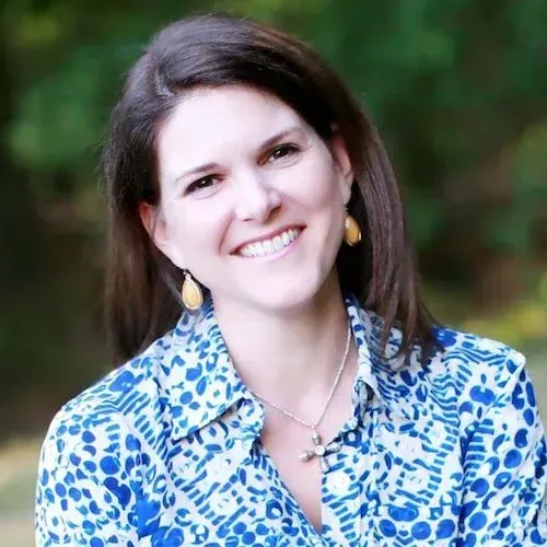 Smiling woman in a blue patterned blouse outdoors with a blurred green background