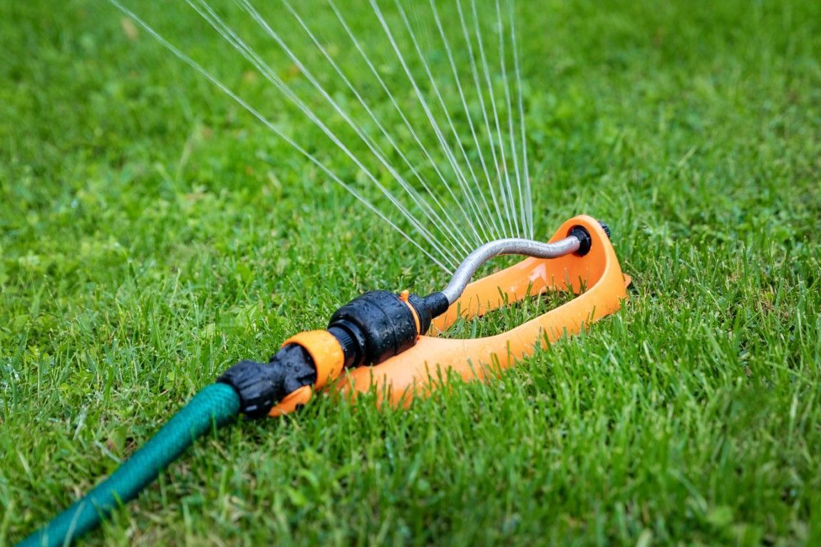 Orange and green garden hose sprinkler spraying water on a grassy lawn