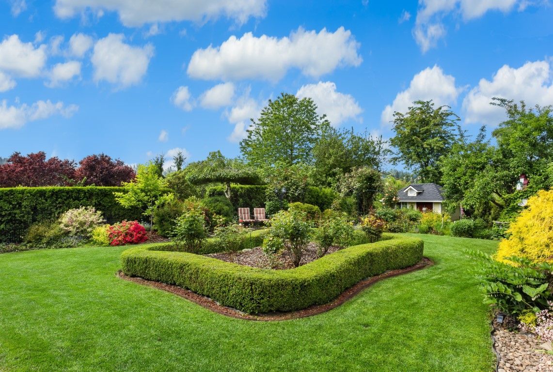 Lush garden with manicured hedges, colorful flowers, and bright green lawn under a blue sky