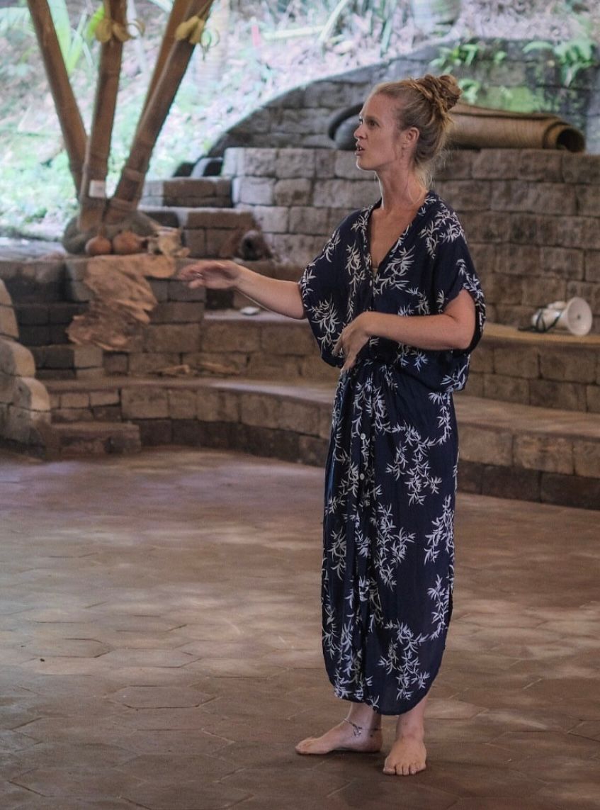 Woman in a navy floral jumpsuit standing in a stone pavilion, gesturing while speaking