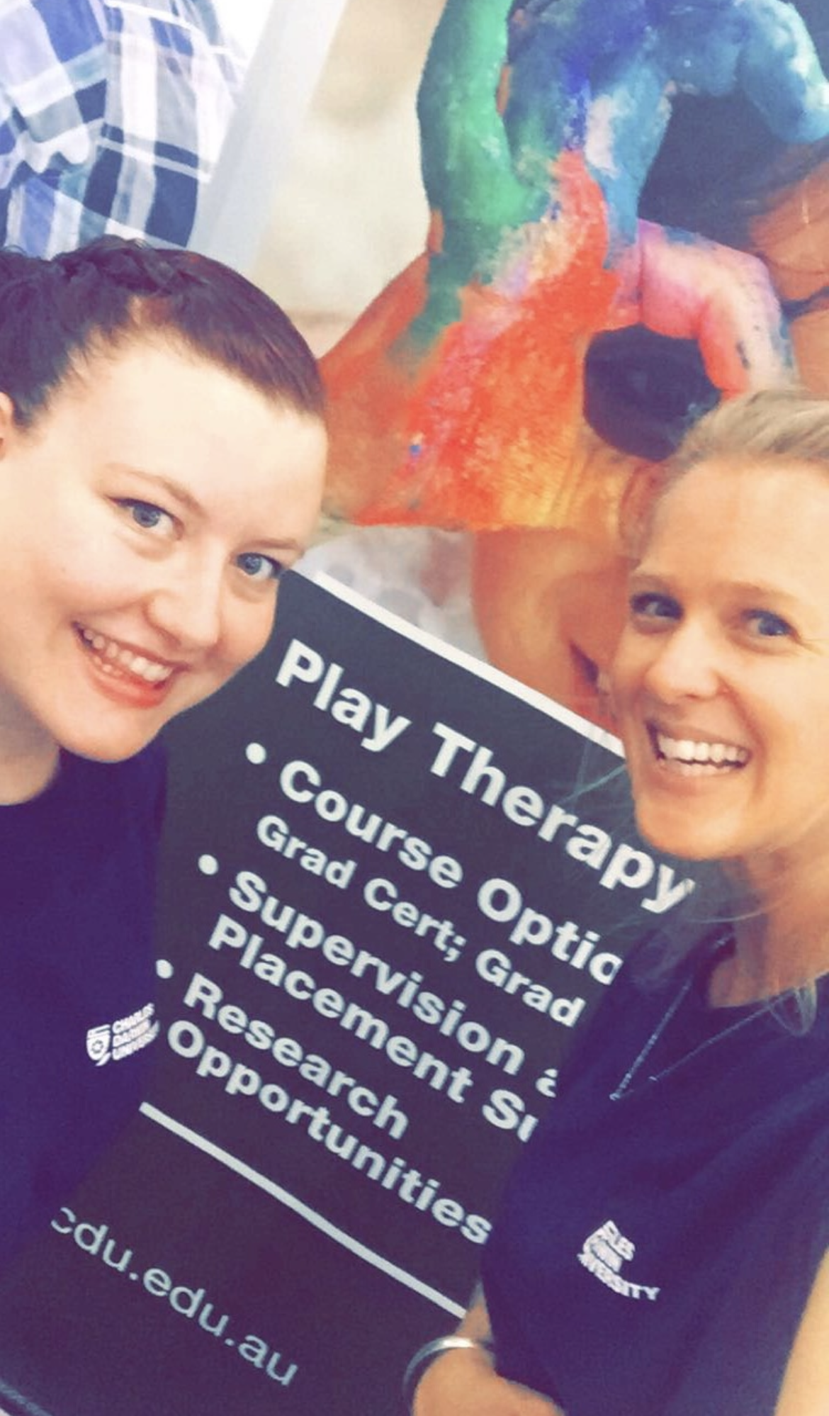 Two smiling women holding a purple Play Therapy brochure at a university event