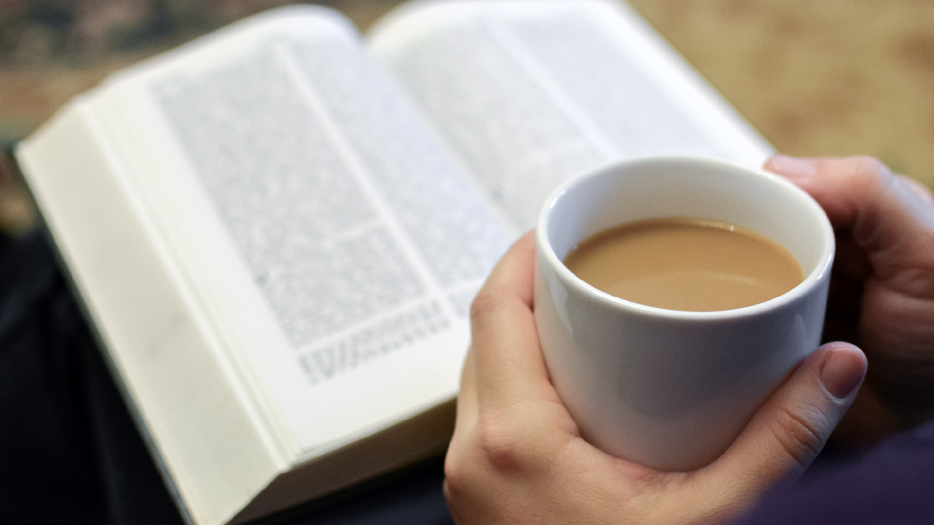 A person is holding a cup of coffee in front of an open book