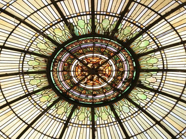 Looking up at a stained glass dome with a clock in the center.