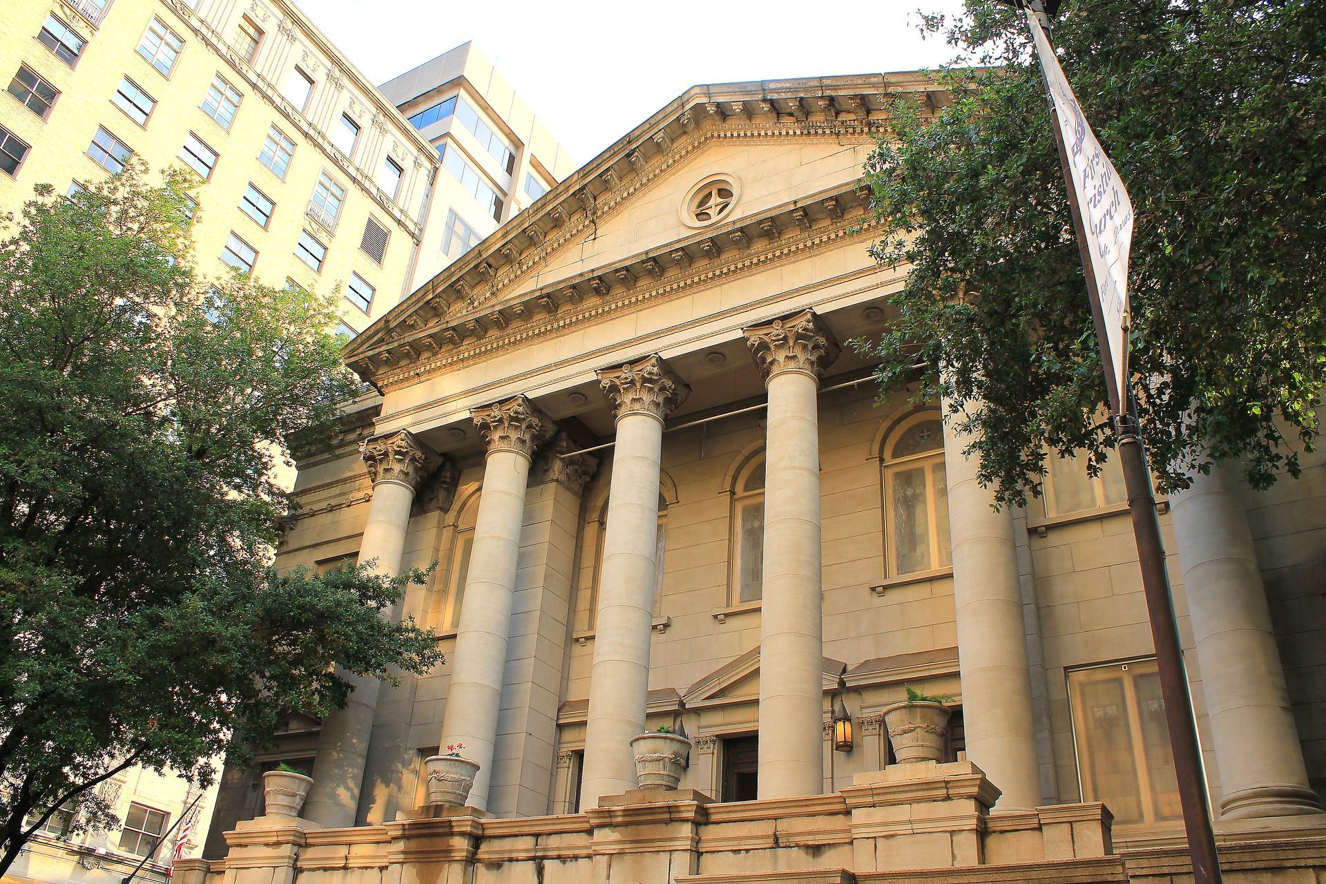 Classical stone building with columns and pediment, partially obscured by trees.