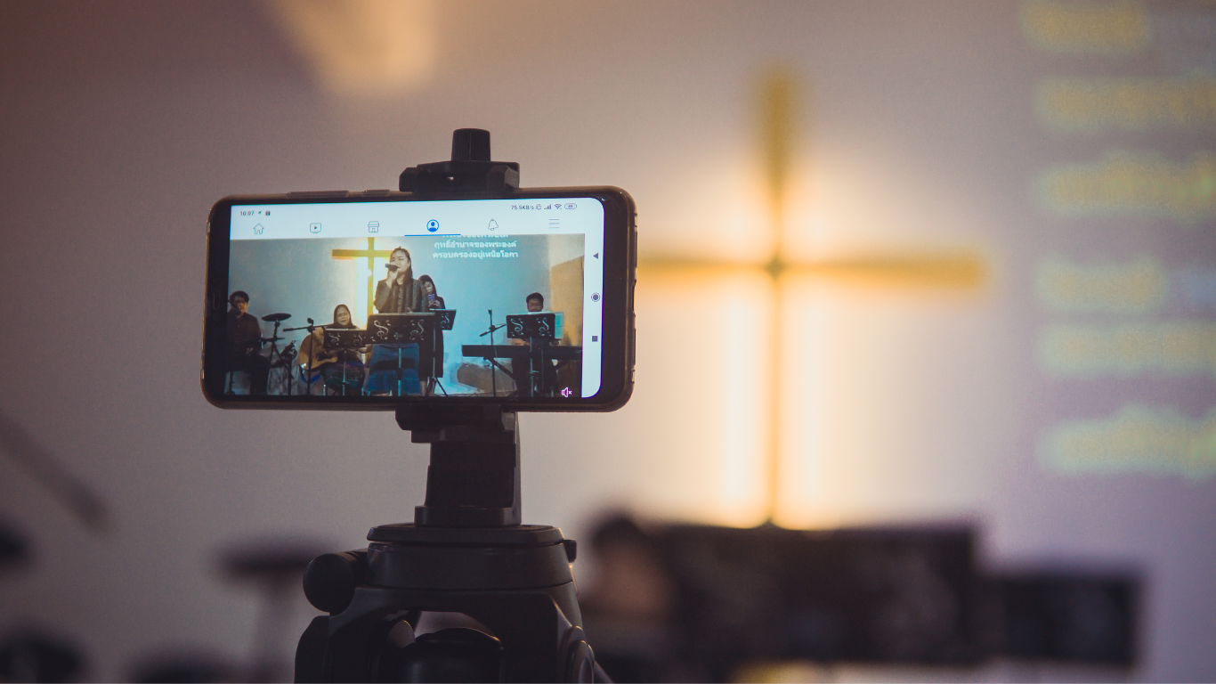 A person is holding a cell phone on a tripod in front of a cross.