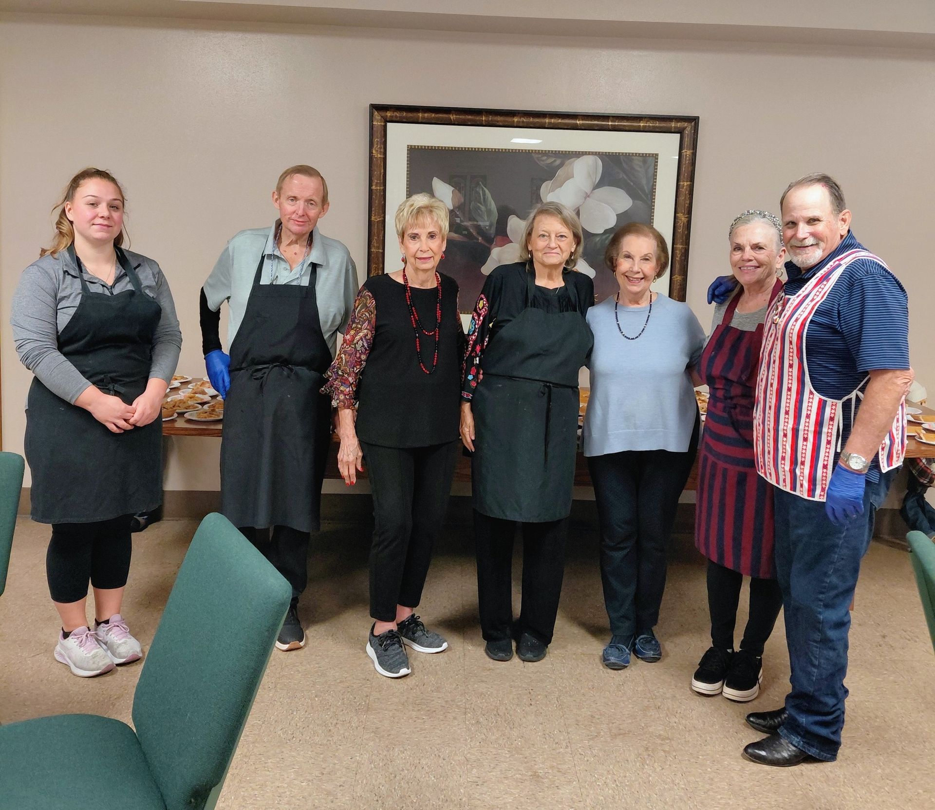 Group of people in aprons, likely volunteers, standing together in a room with a painting.
