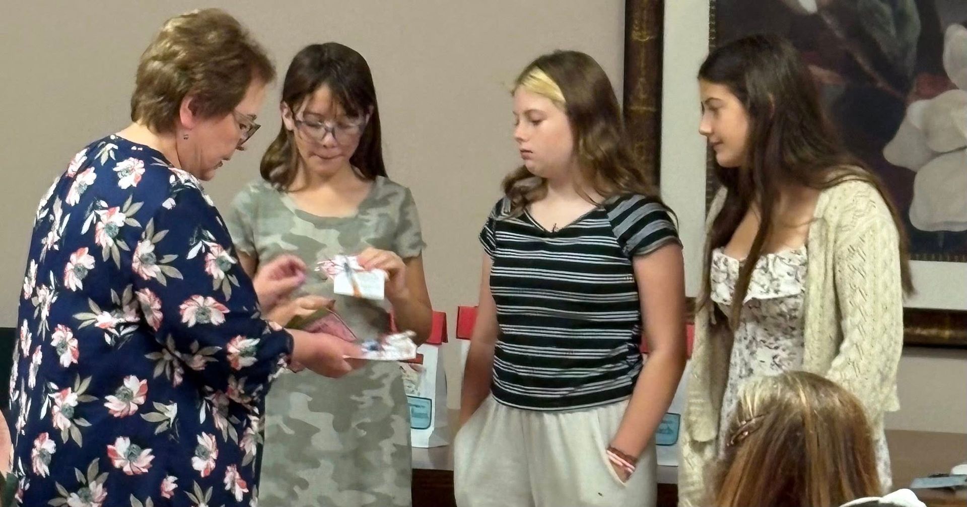 Woman showing papers to three young people indoors; all looking at the papers.