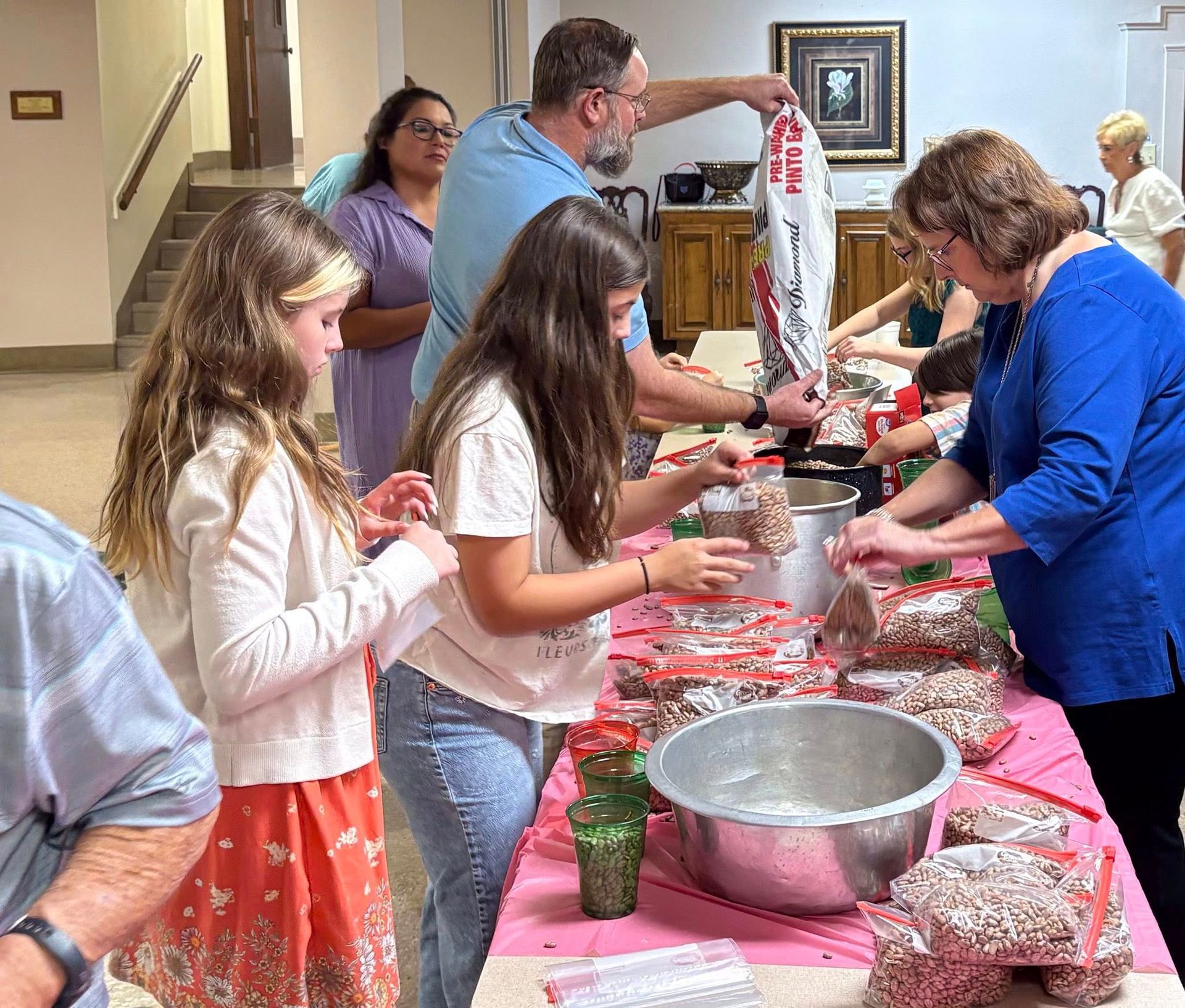 People packing items at a table. Bags, containers, and a silver bowl are visible.