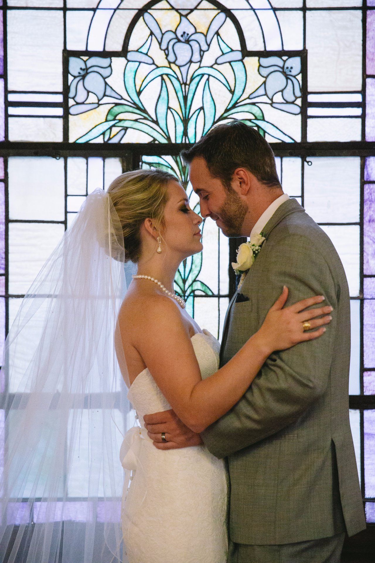 A bride and groom are kissing in front of a stained glass window.