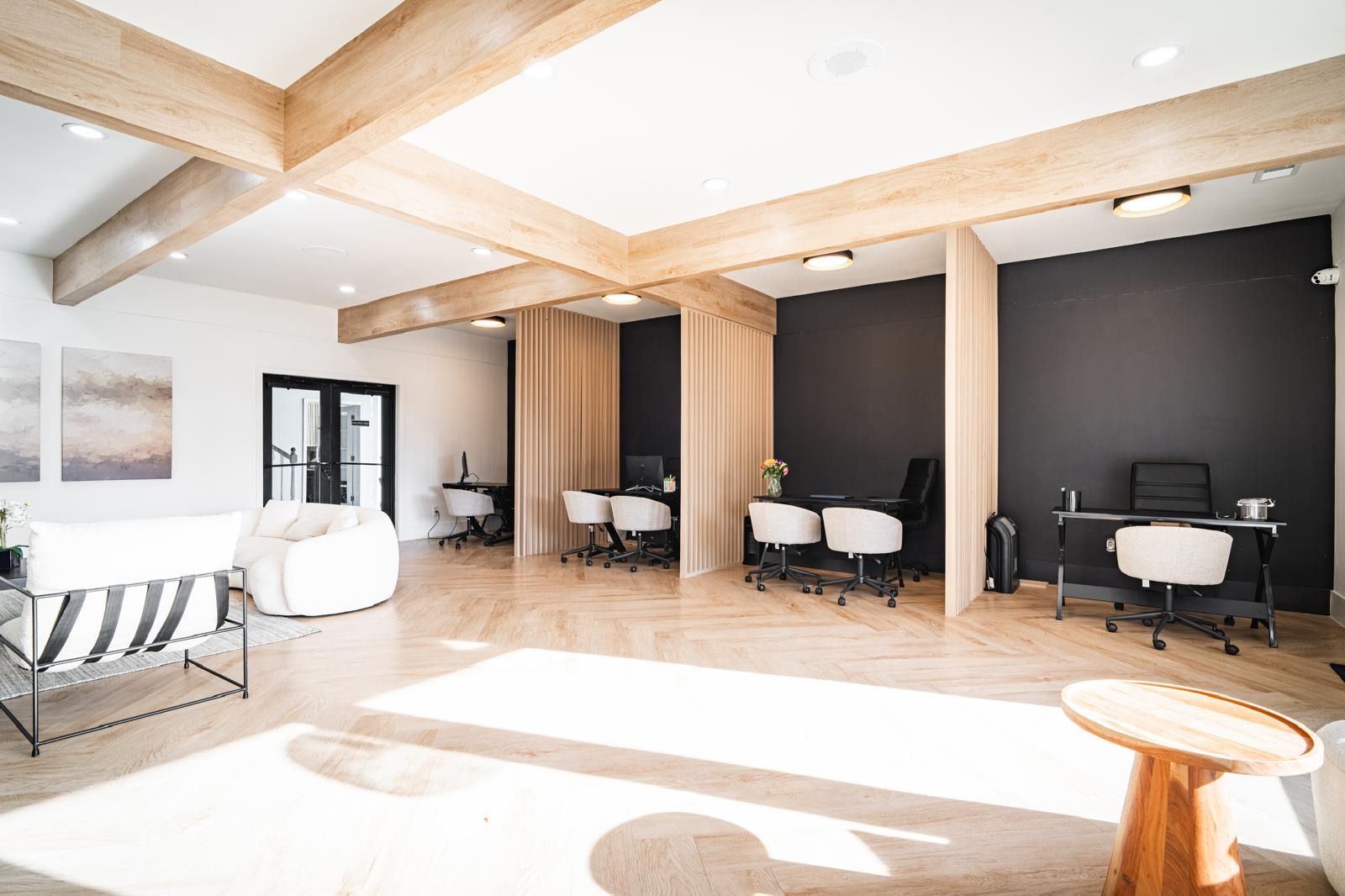 Bright modern salon with white chairs, black walls, and wooden beams in a sunlit open room
