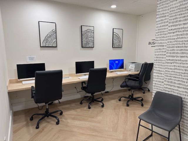 Quiet computer lab with desks, black chairs, monitors, and framed wall art.