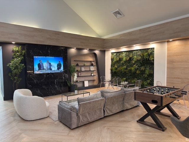 Modern lounge with sectional sofa, armchair, TV, shelving, and a foosball table beside a green wall.