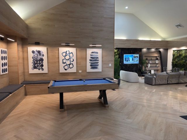 Modern lounge with a pool table, wall art, TV, and gray sectional seating under warm wood ceilings