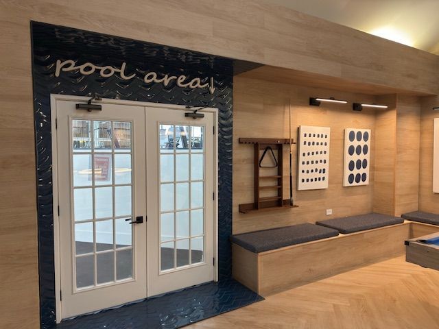 Indoor pool area entrance with glass doors, dark blue trim, and wooden walls with seating and wall art