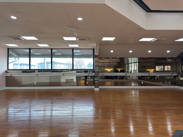 Empty indoor hall with polished wood floor, large windows, and bright ceiling lights