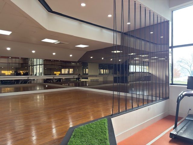 Empty indoor gym with polished wood floor, mirror wall, and cardio equipment on the right