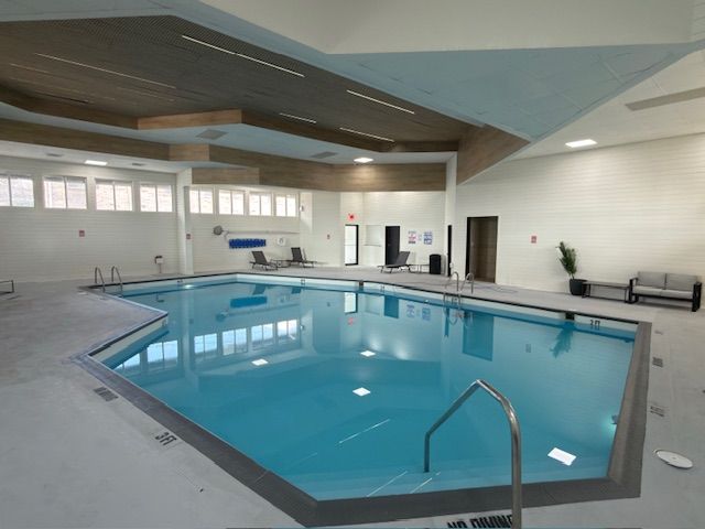 Indoor swimming pool with blue water, white walls, and a diving board area under a wood-paneled ceiling