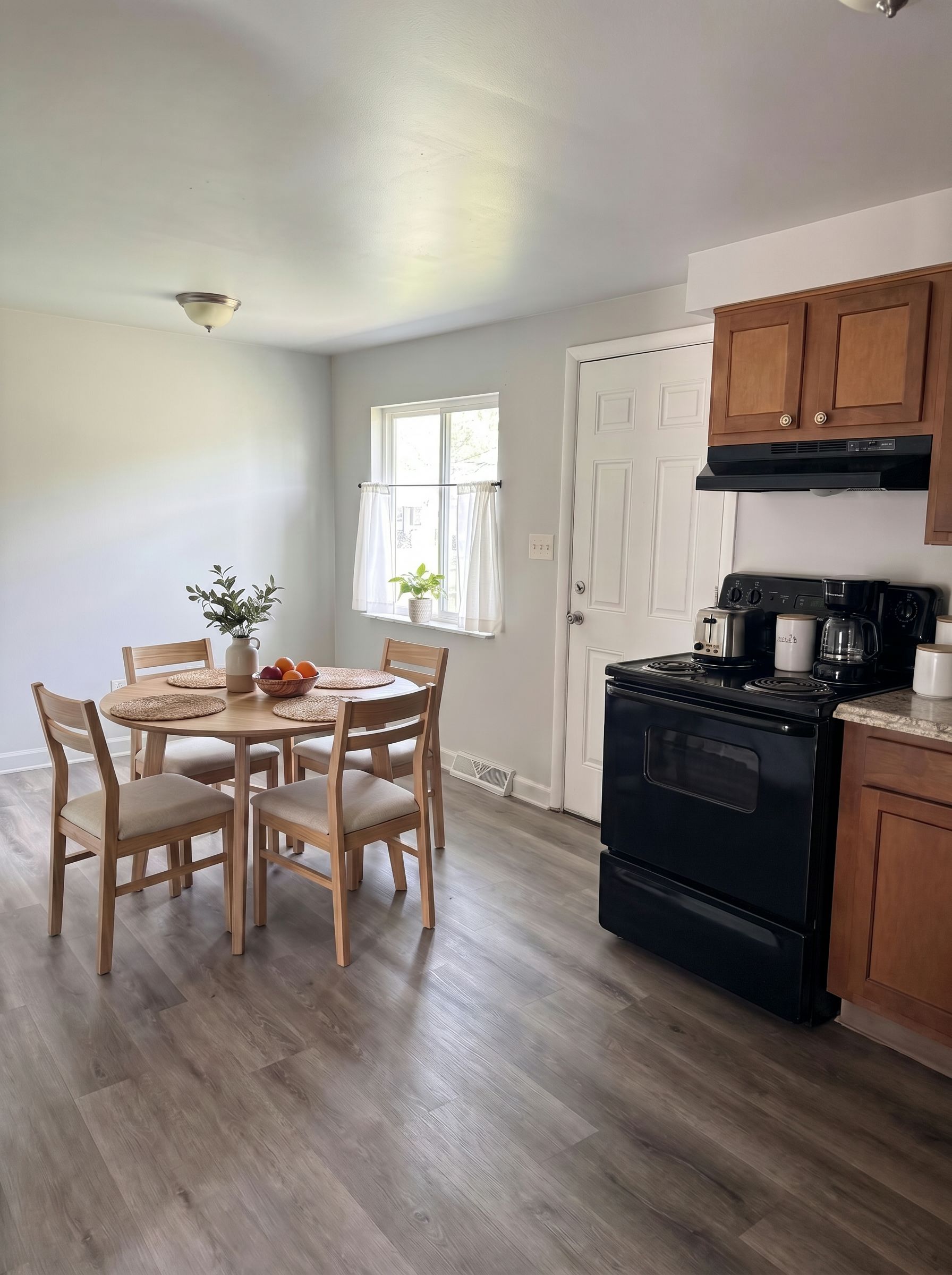 Small dining area with wooden table, chairs, black stove, and brown cabinets in a bright kitchen.