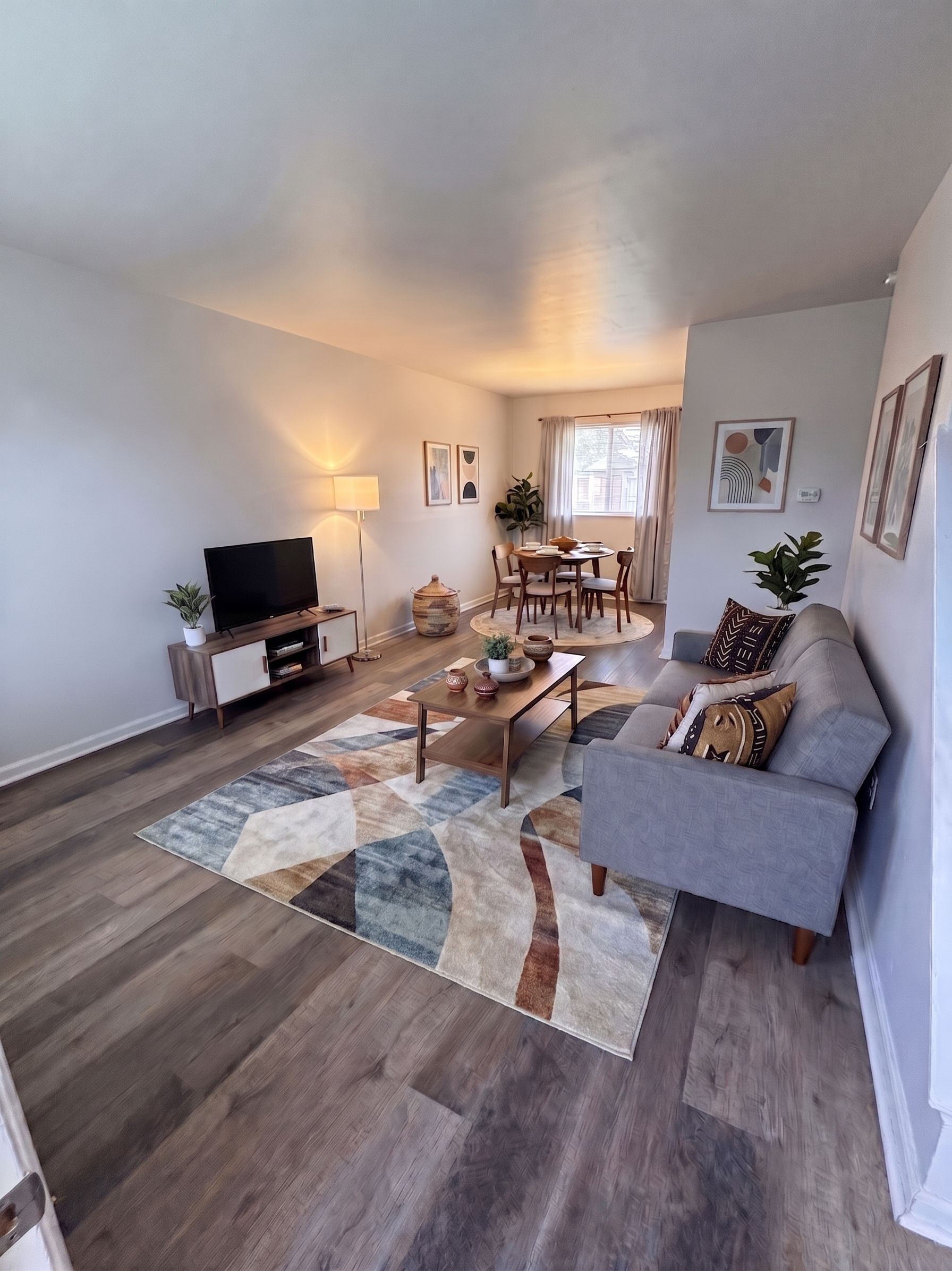 Modern living room with gray sofa, patterned rug, coffee table, TV, and warm wall lighting
