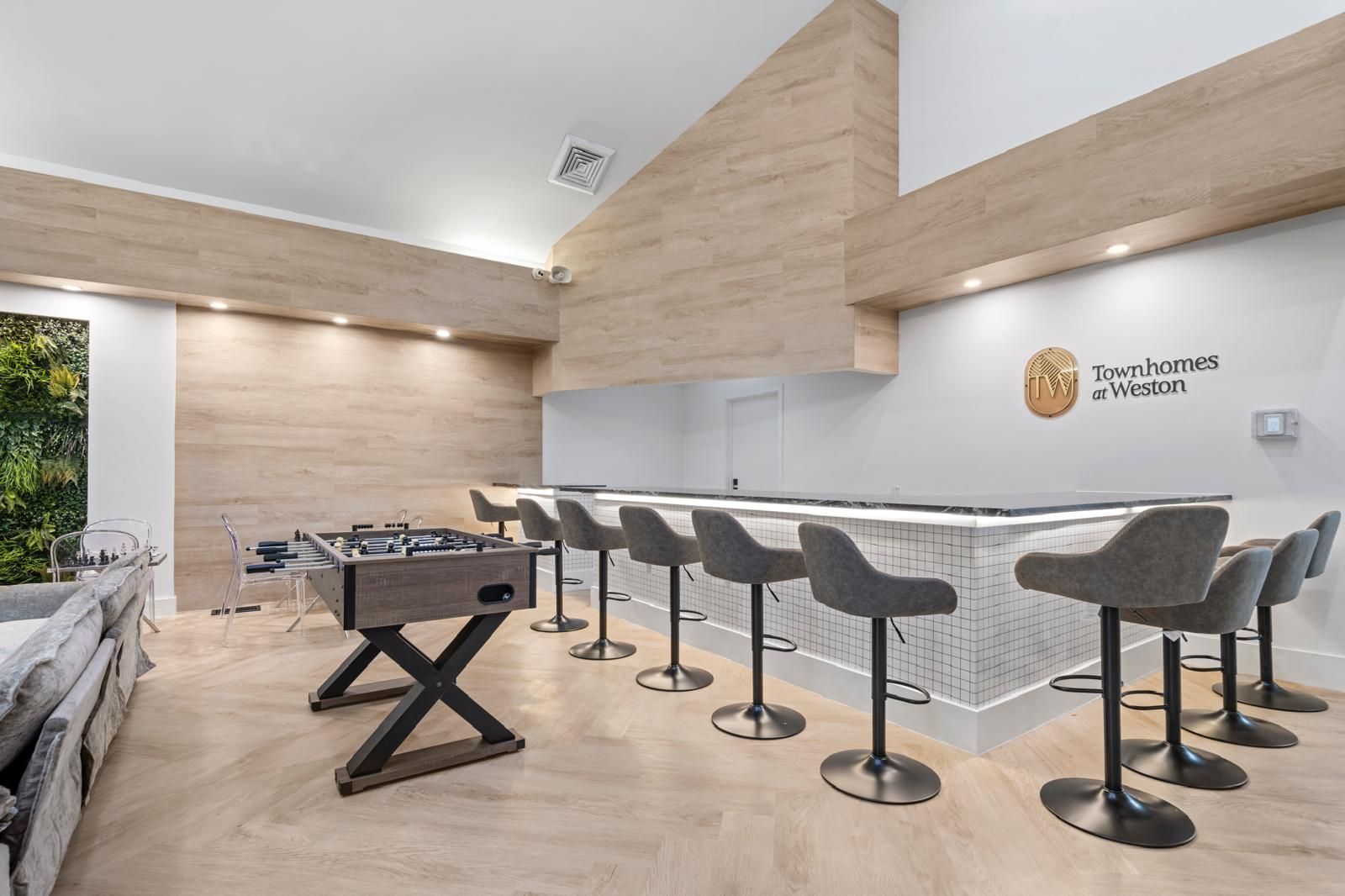 Modern kitchen lounge with island seating, wood accents, and a pool table by large windows