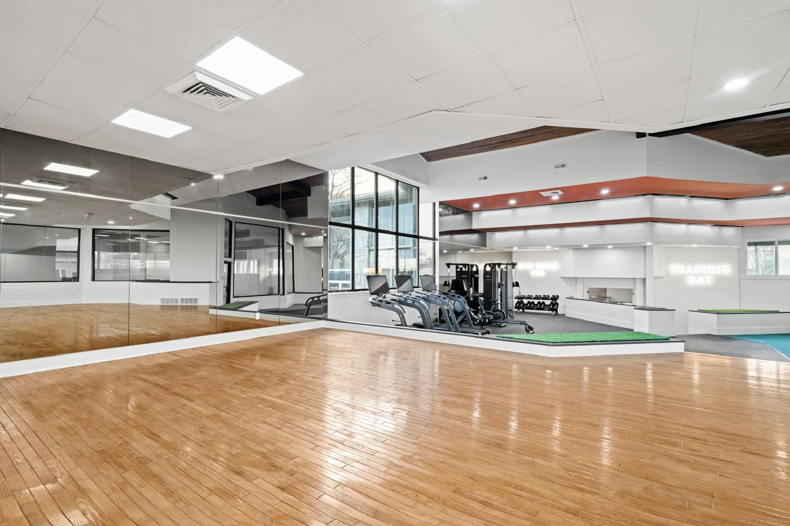 Empty modern gym with wood floor, exercise machines, mirrors, and glass-walled studio area