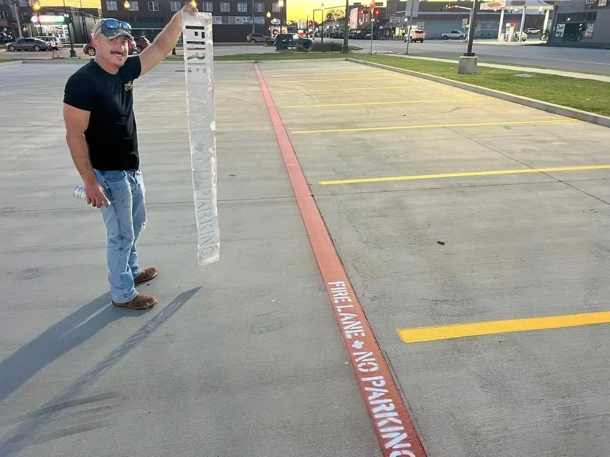 Zach of AcePavement Solutions holding a fire lane stencil after application at ABC Auto Parts in Mineola