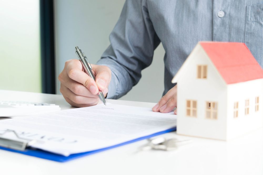 Person Signing Document Next to a Model House — Precision Financial & Tax In Ross Creek, VIC
