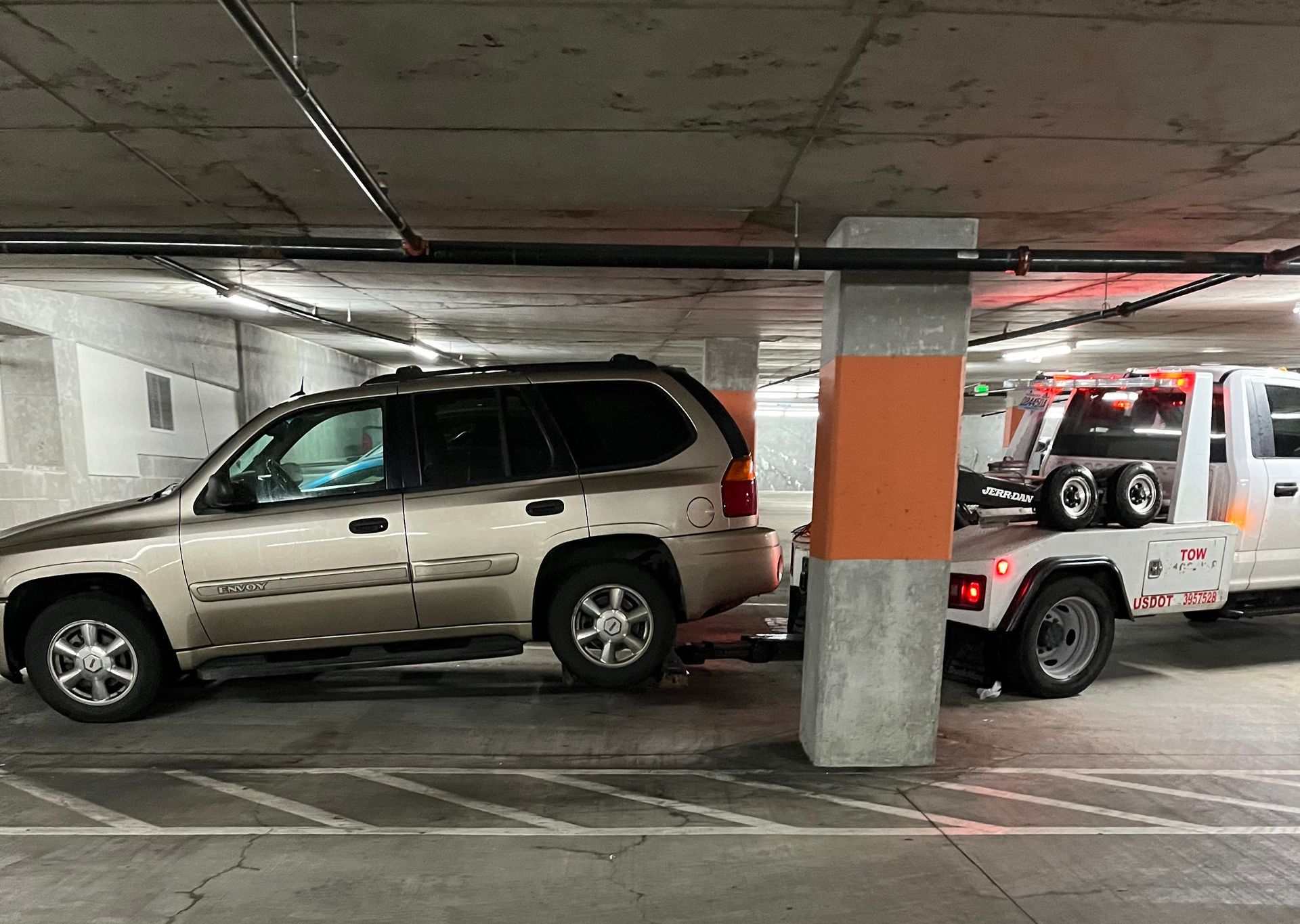 A tow truck is towing a car in a parking garage.