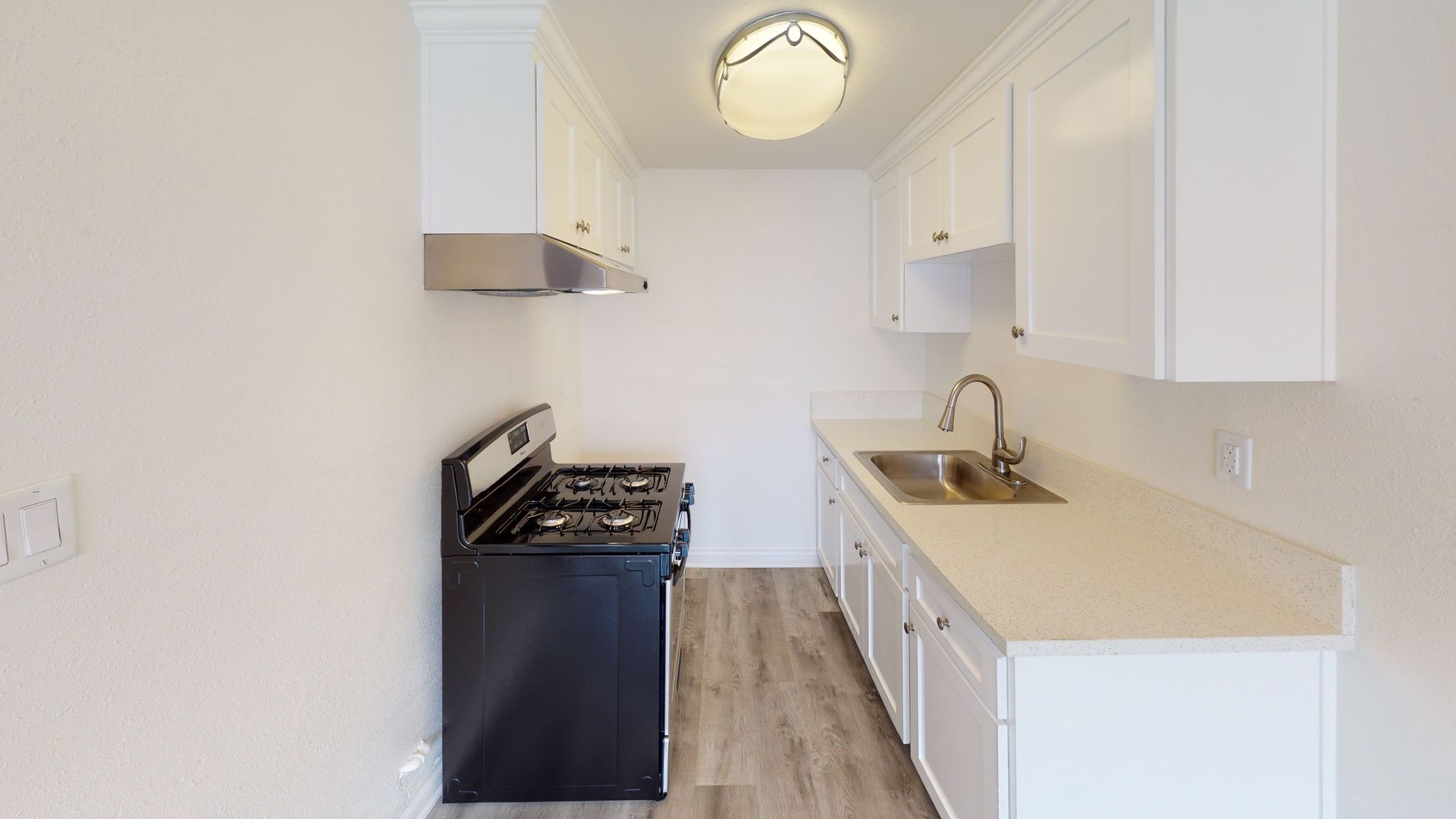 Small white kitchen with black stove, light countertops, and wooden floors.