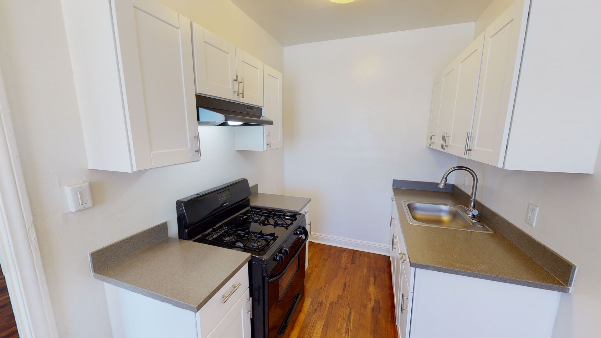 Small kitchen with white cabinets, dark stove, and gray countertops.