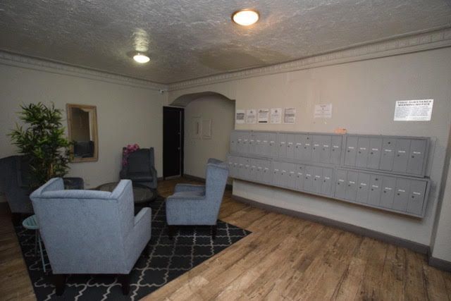 Lobby with seating area and mailboxes. Light blue chairs, wooden floor, gray walls, and bright lighting.