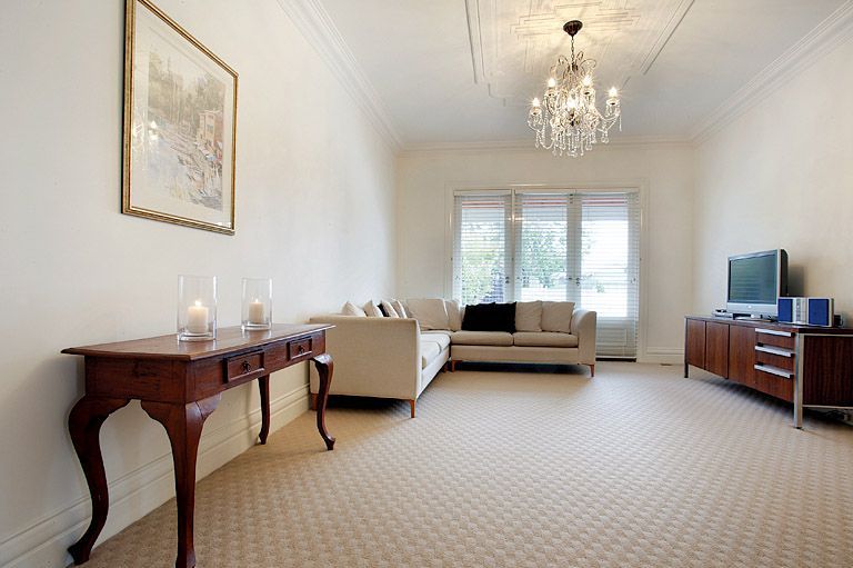 Bright living room with beige sofa, chandelier, sideboard, TV, and patterned carpet. — KM Custom Homes In Mornington, VIC